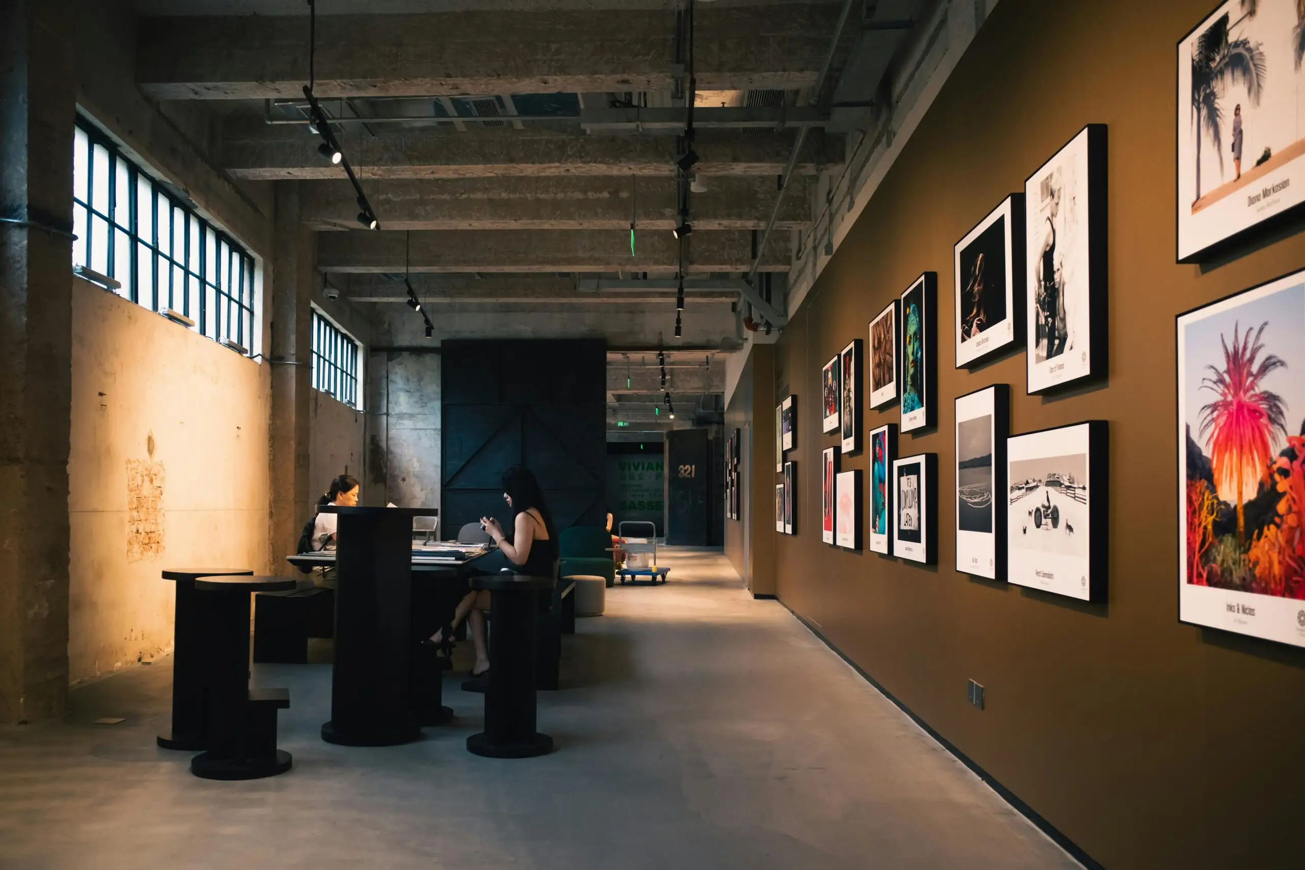 Et si votre entreprise devenait une galerie d’art ? Art gallery hallway with framed artworks and visitors seated inside, under warm lighting.
