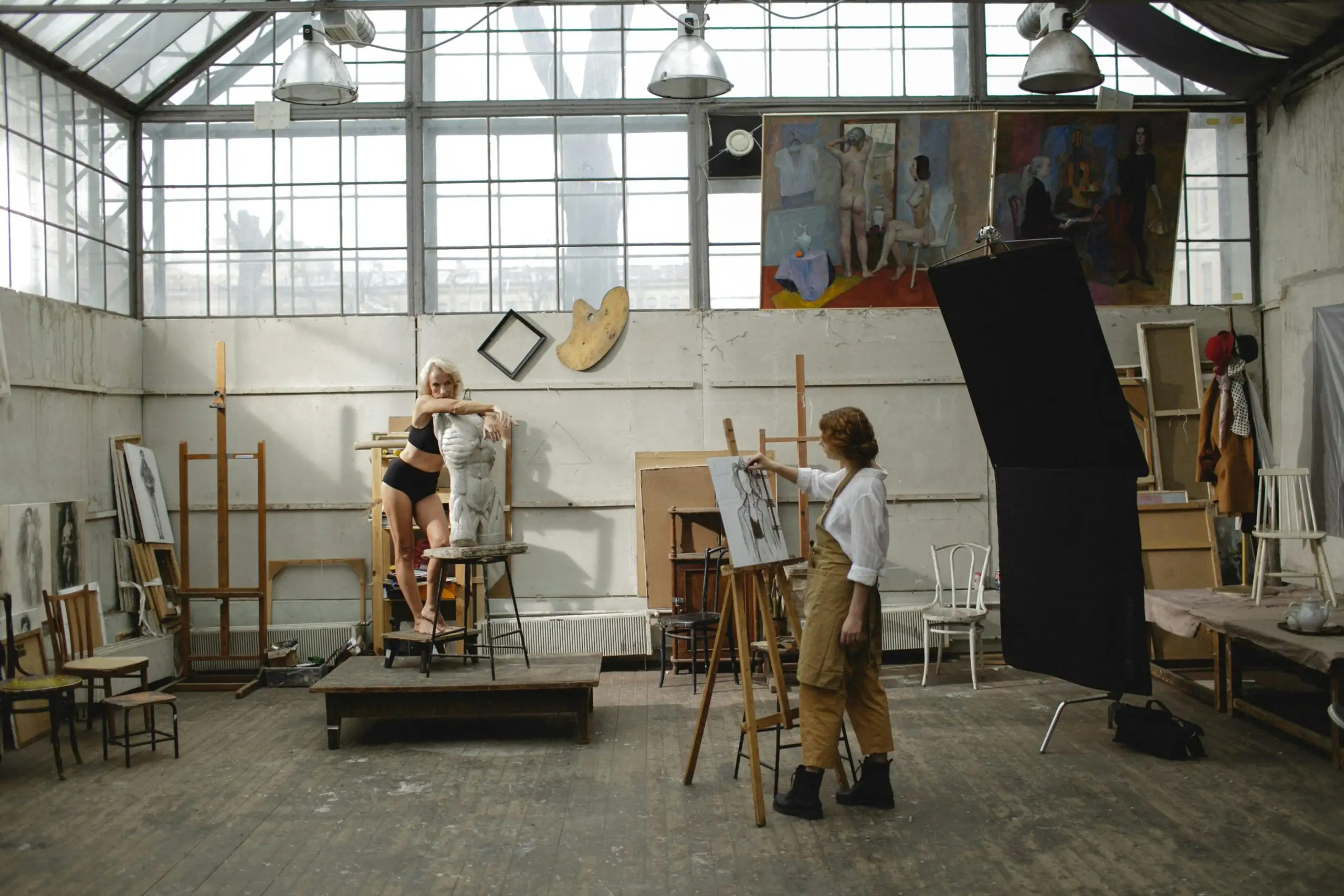 Artistes : et si votre atelier devenait un point central de la scène locale ? Art studio scene featuring an artist drawing a live model on an easel, showcasing creativity.